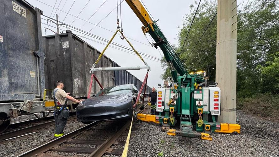 Tesla Model 3 being lifted off train tracks with a crane.
